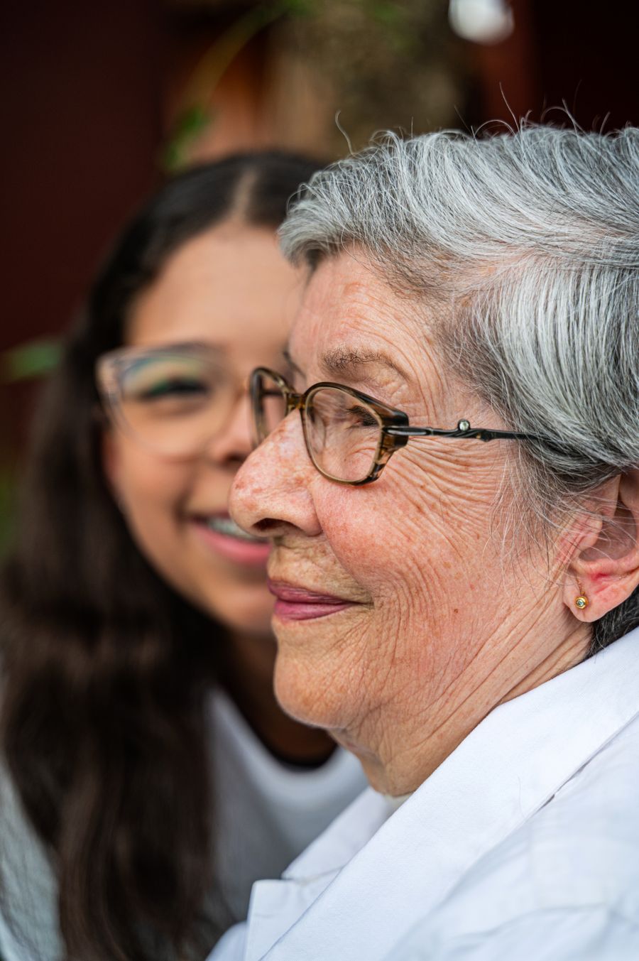 A younger woman standing close behind an older woman, both smiling
