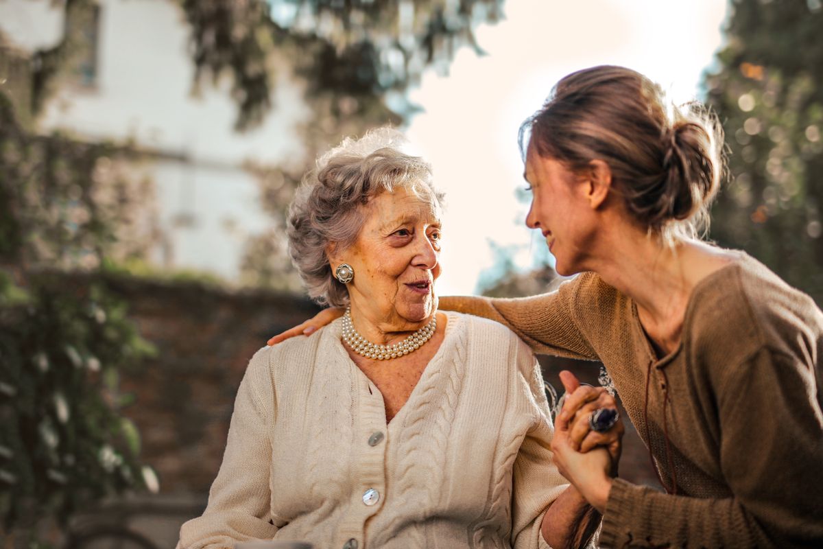 A younger woman sitting with an older woman, a hand resting on her shoulder